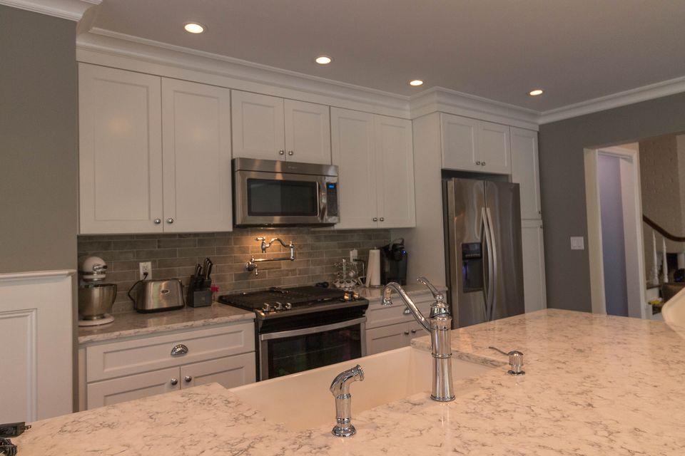 White kitchen with a quartz island, stainless appliances, and recessed lighting